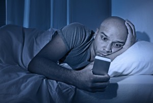 young cell phone addict man awake at night in bed using smartphone for chatting flirting and sending text message in internet addiction and mobile abuse concept